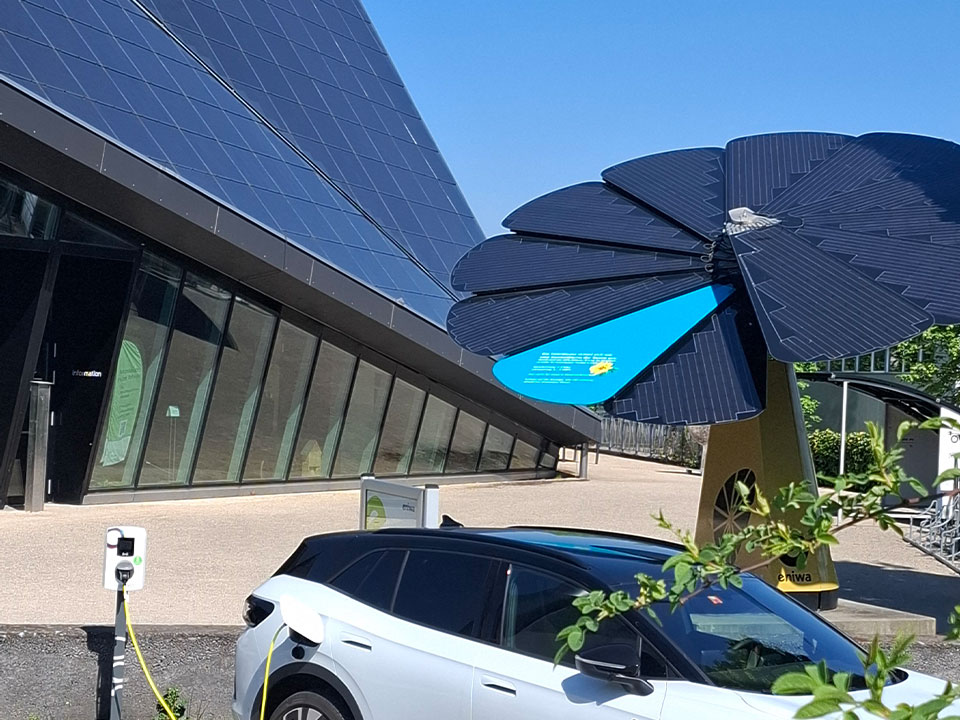 Bildausschnitt der Umwelt Arena von aussen, mit weissem Elektroauto welches gerade an einer Ladestation lädt, Solarblume und Photovoltaik-Anlage des Gebäudes